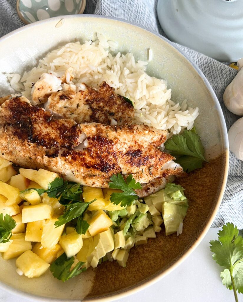 Blackened tilapia in a bowl with pineapple and avocado. 