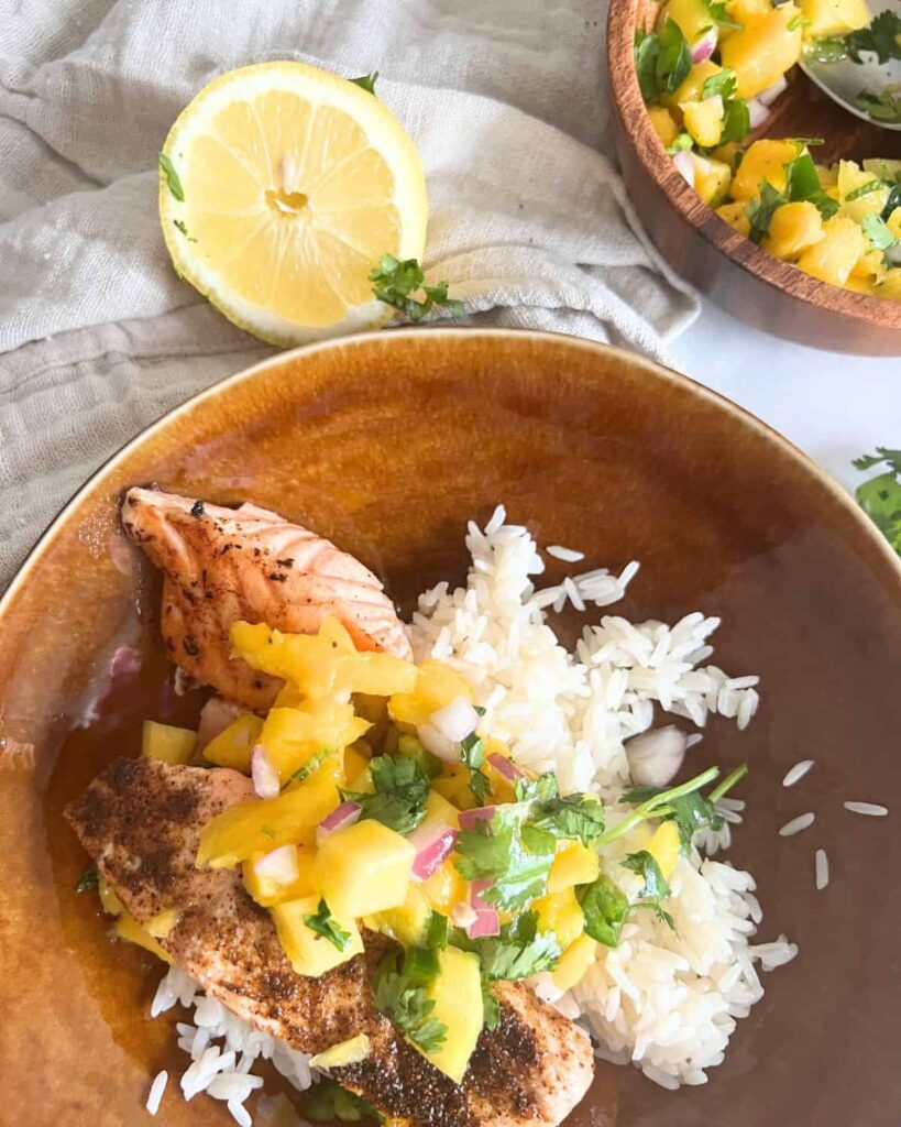 Blackstone salmon topped with mango salsa and white rice in a bowl. 