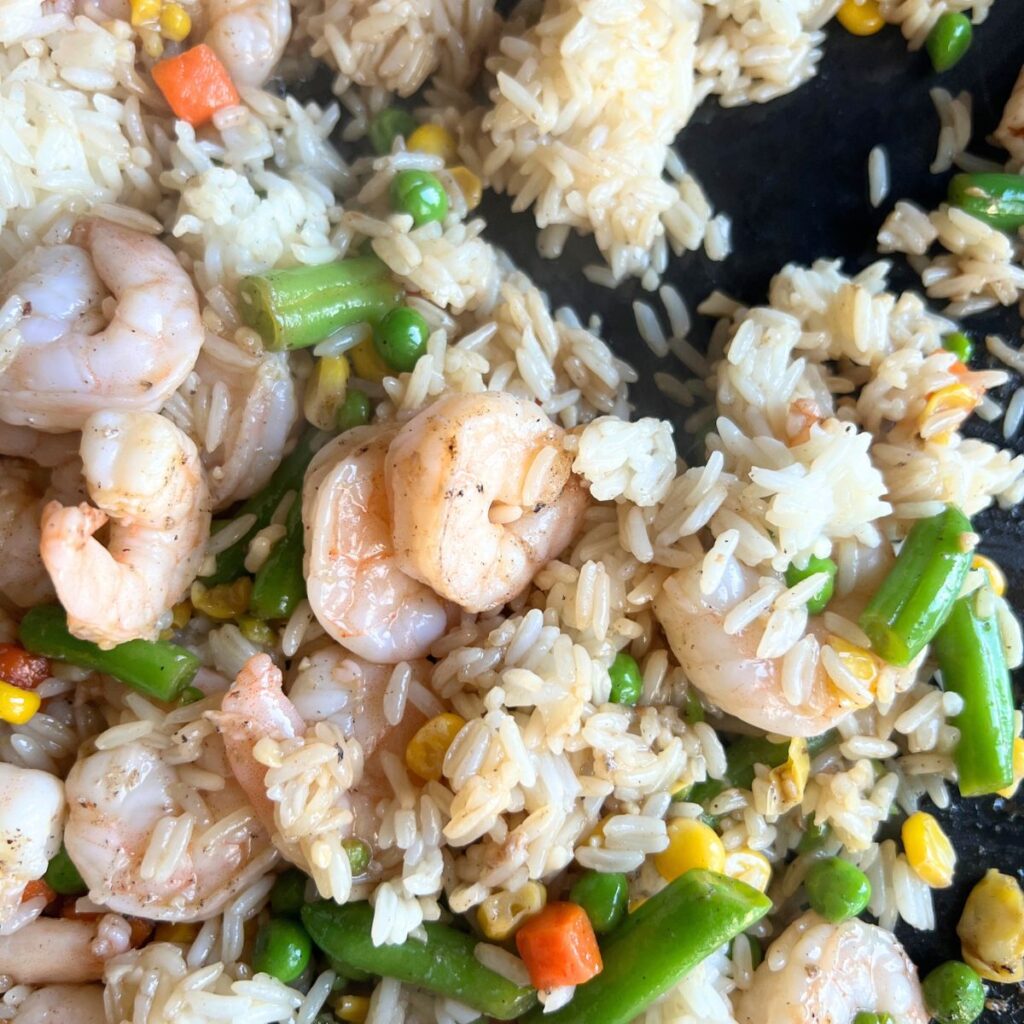 Shrimp, vegetables, and rice cooking on a griddle. 