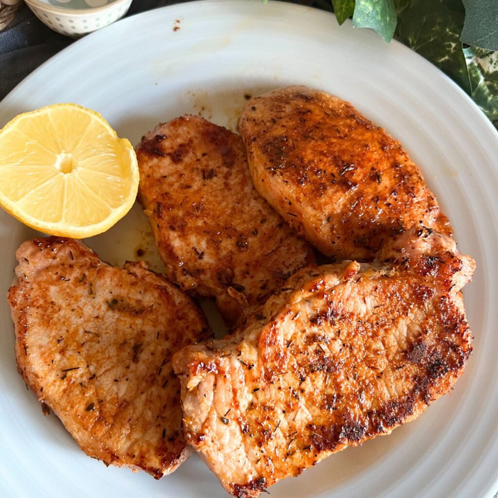 Seasoned cooked pork chops on a white plate next to a lemon. 